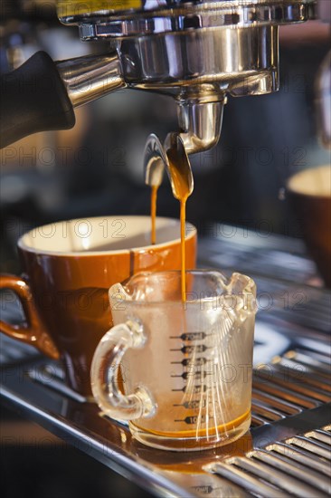 Coffee pouring from portafilter into coffee cup and beaker