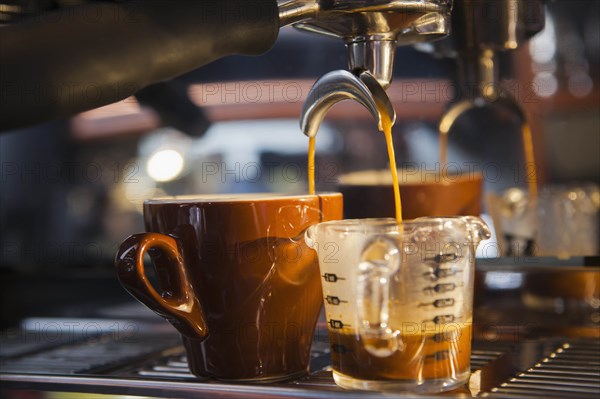 Coffee pouring from portafilter into coffee cup and beaker