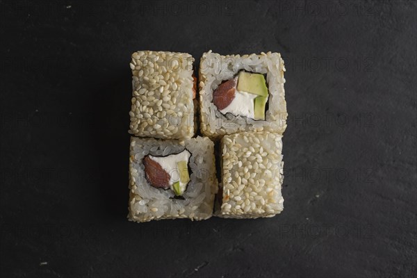 Sushi with sesame seeds on black surface
