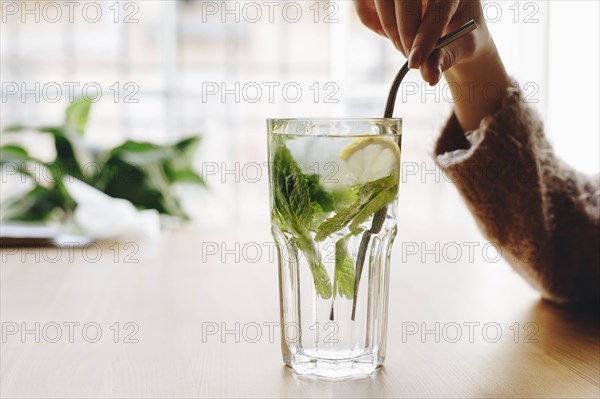 Woman holding straw in cocktail with mint leaves and lemon