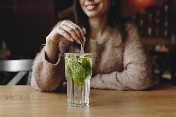 Woman holding straw in cocktail with mint leaves