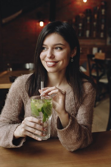 Woman holding straw in cocktail with mint leaves