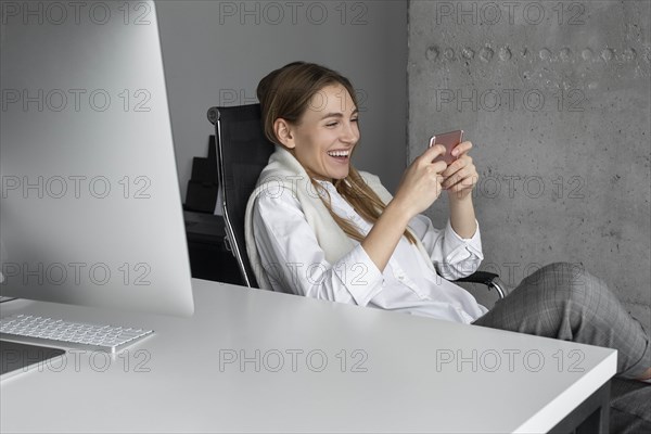 Laughing businesswoman using smartphone at desk