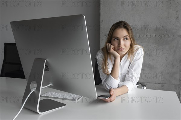 Businesswoman with smartphone day dreaming at desk