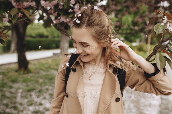 Smiling woman among falling petals from tree in bloom