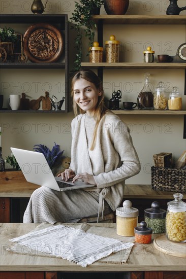 Smiling young woman using laptop in kitchen