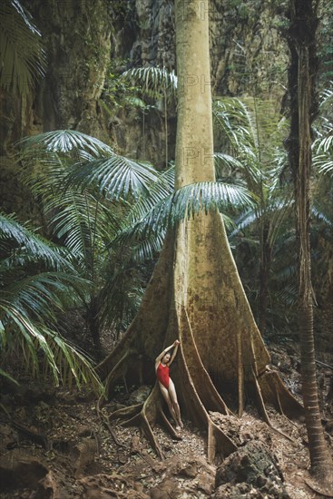 Young woman in swimsuit leaning on large tree in Krabi, Thailand