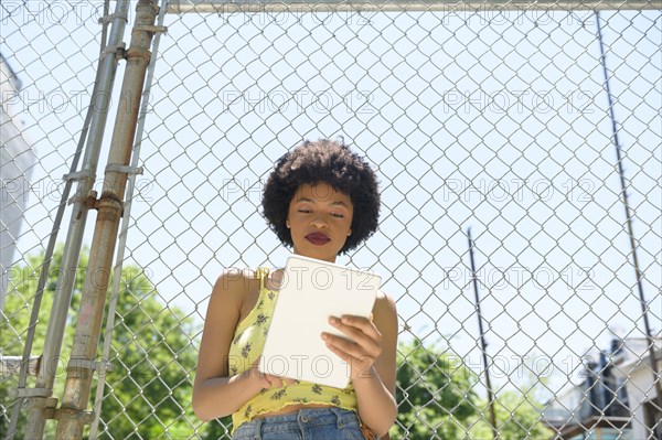 Young woman using digital tablet by wire fence