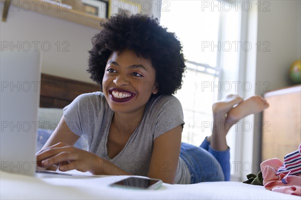 Smiling young woman lying on bed using laptop