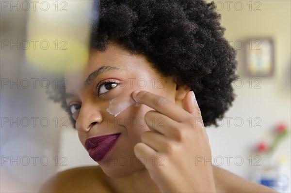 Young woman applying moisturizer to her face