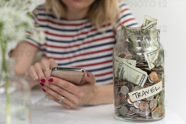 Woman using smart phone by travel saving jar