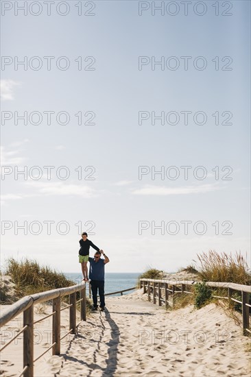 Father helping his son walking on fence on beach