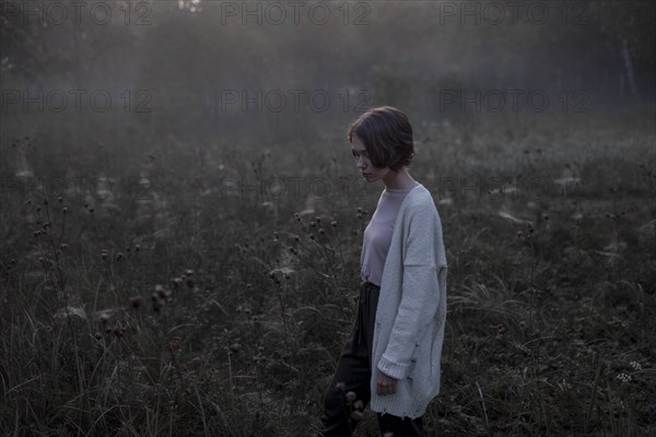 Young woman wearing white cardigan in field at sunset