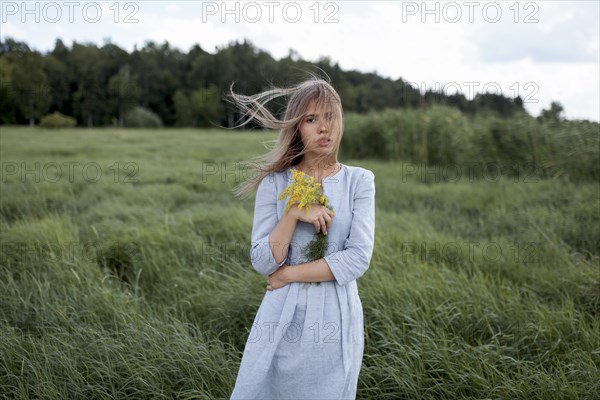 Windswept woman holding yellow flowers in field