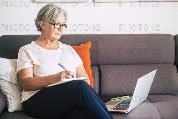 Senior woman holding pen using laptop on sofa