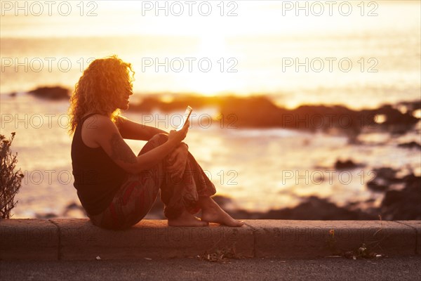 Woman using smart phone by beach at sunset