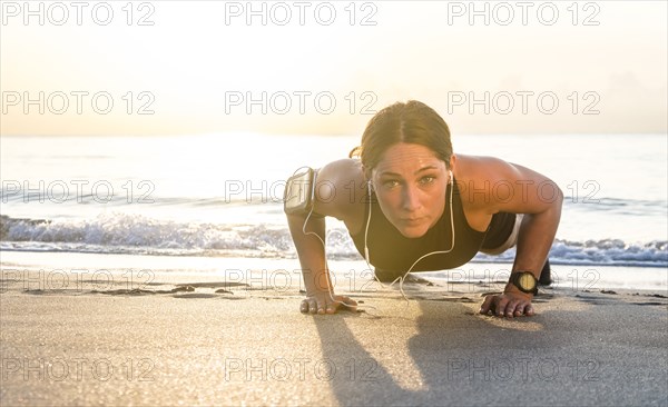 Woman wearing headphones doing push-up on beach