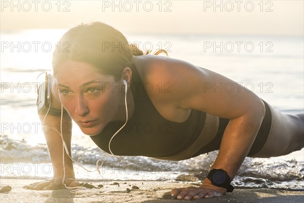 Woman wearing headphones doing push-up on beach