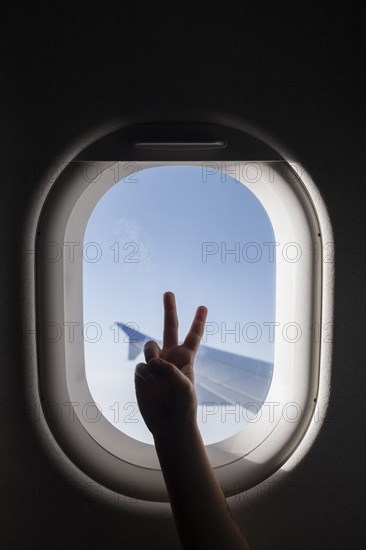 Silhouette of girl's hand doing peace sign by airplane window