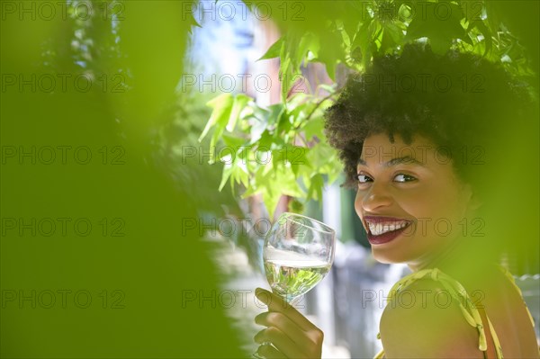 Smiling young woman with glass of white wine under tree