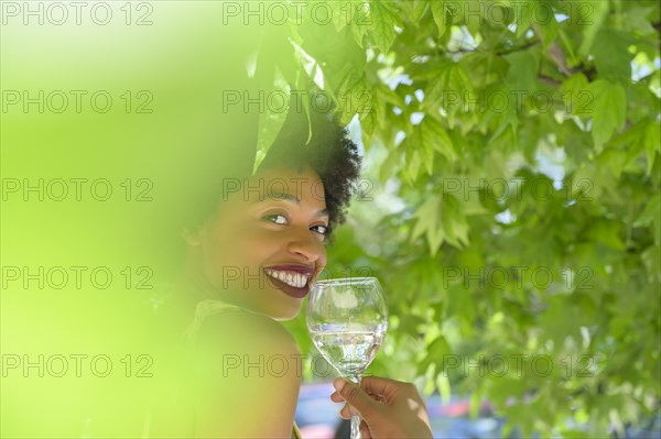 Smiling young woman with glass of white wine under tree