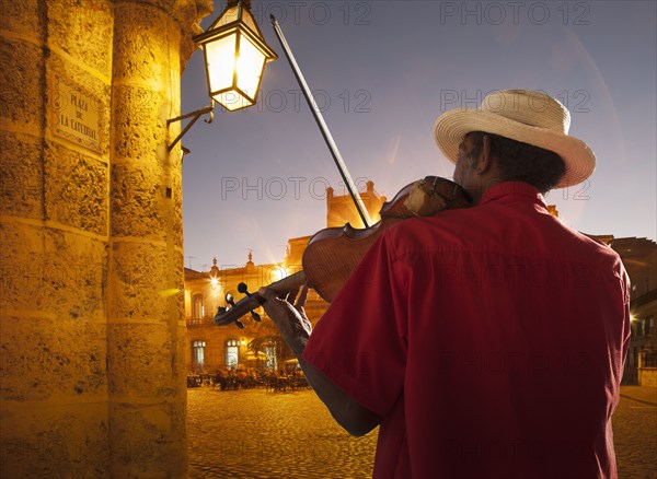 Senior man playing violin at night in Plaza de la Catedral, Havana, Cuba