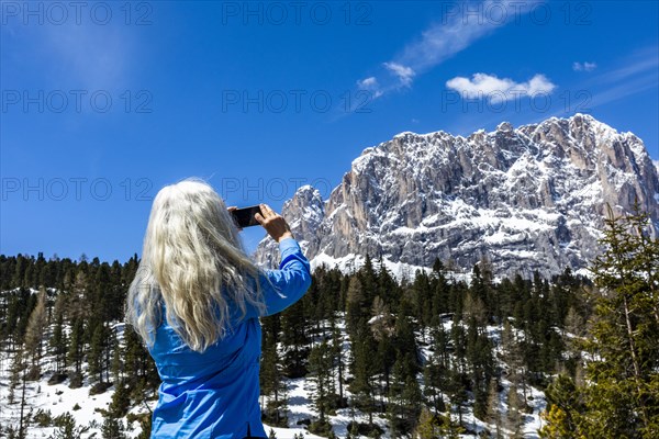 Woman taking photograph with smart phone by mountain in Dolomites, Italy