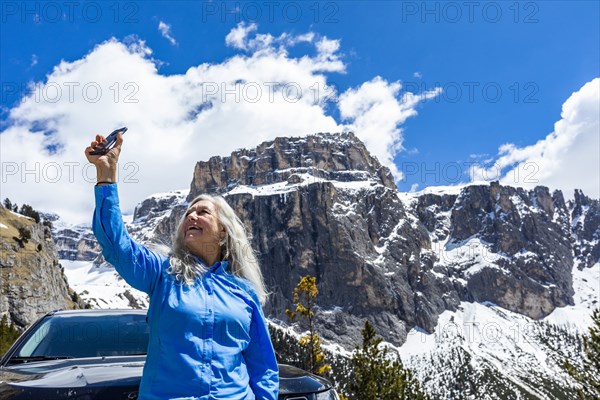 Woman taking photograph with smart phone by mountain in Dolomites, Italy