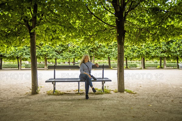 Woman on park bench by trees in Palais-Royal gardens in Paris, France