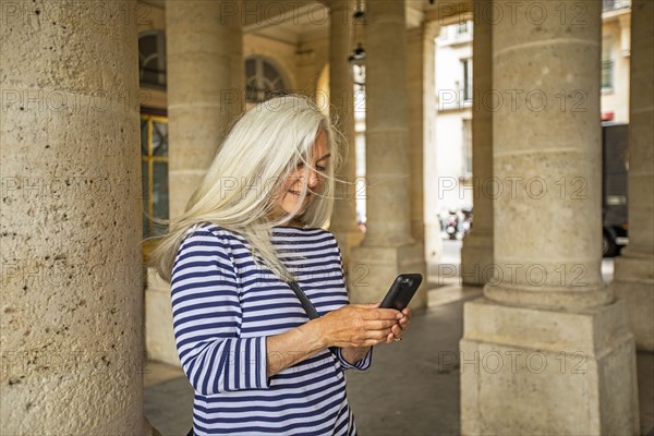 Woman using smart phone by columns of Palais-Royal in Paris, France