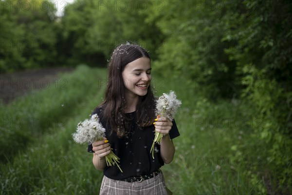 Smiling teenage girl holding dandelions in a field