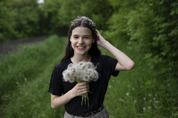 Smiling teenage girl holding dandelions in a field