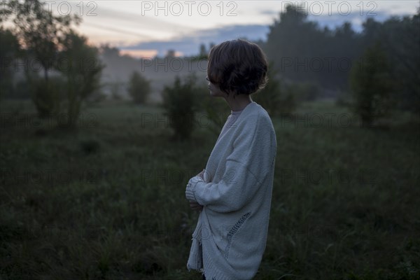 Young woman wearing white cardigan in field at sunset