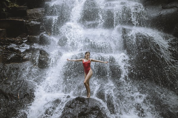 Woman wearing red swimsuit by waterfall in Bali, Indonesia