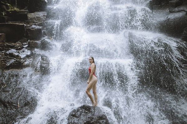 Woman wearing red swimsuit by waterfall in Bali, Indonesia