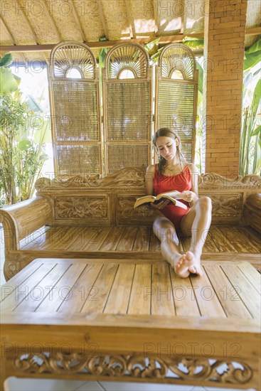 Woman wearing swimsuit reading book on wooden sofa
