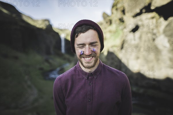 Smiling man with flowers on his face by Kvernufoss waterfall in Iceland