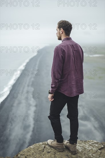 Man wearing purple shirt above beach in Vik, Iceland