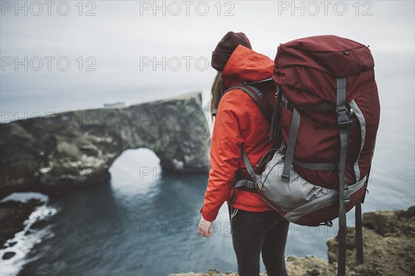 Female hiker wearing red by natural arch in Vik, Iceland