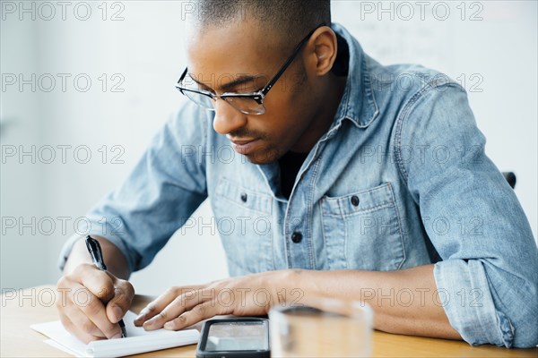 Man wearing glasses writing on note pad