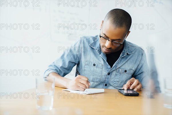Man using smart phone while writing on note pad