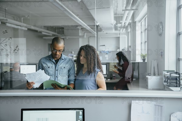 View through window of coworkers reading documents in office