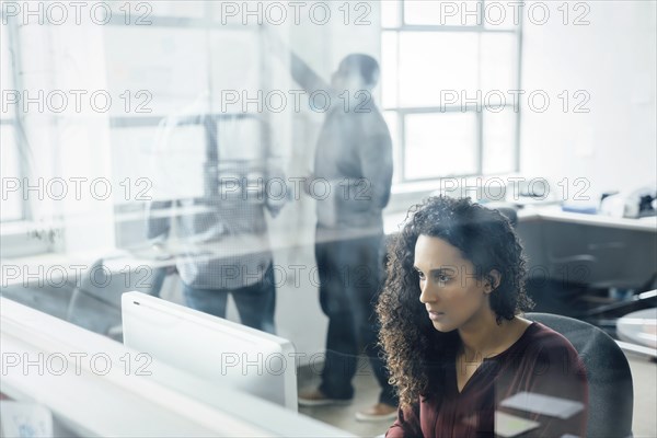 View through window of woman using computer in office