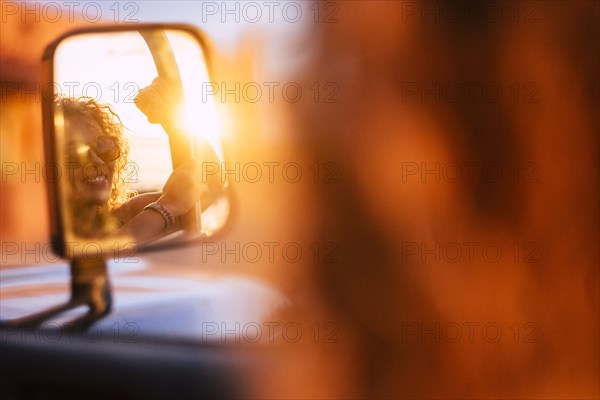 Reflection in wing mirror of smiling woman wearing sunglasses