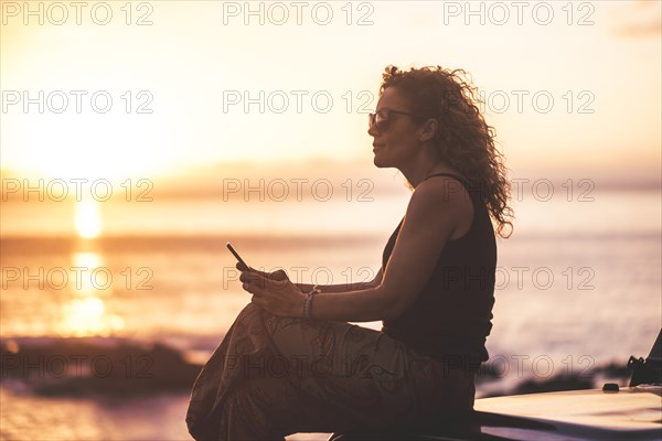 Woman using smart phone by beach at sunset