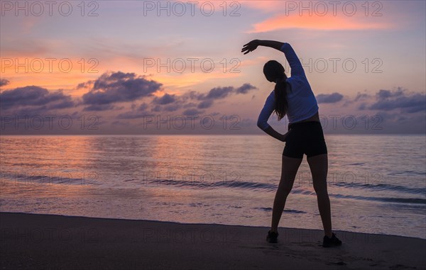 Woman practicing yoga on beach at sunset