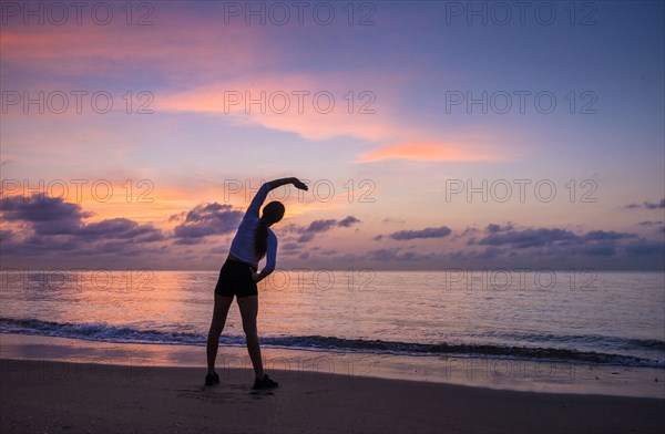 Woman practicing yoga on beach at sunset