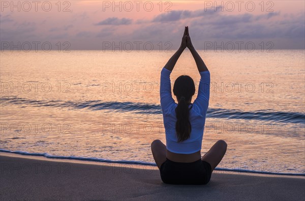 Woman practicing yoga on beach at sunset