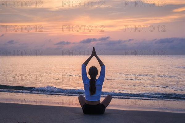 Woman practicing yoga on beach at sunset