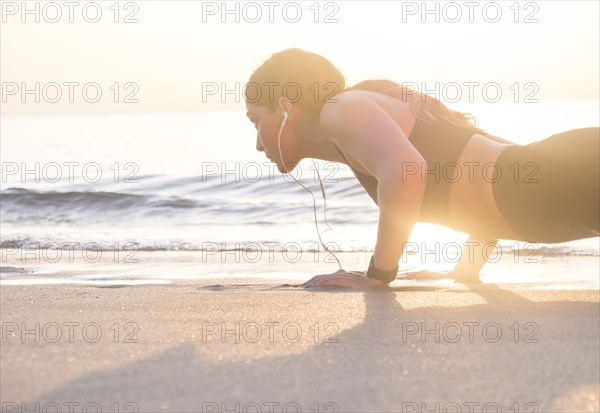 Woman wearing headphones doing push-up on beach